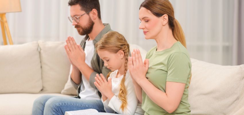 Peaceful family of three praying together on a sofa with hands clasped, perfect for a new year prayer for family moment of faith and unity.