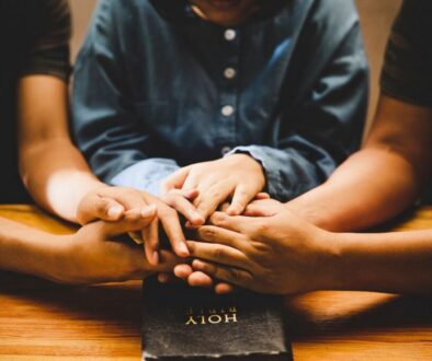 Close-up of family hands joined together in prayer over a Holy Bible, symbolizing love and togetherness in a new year prayer for family.