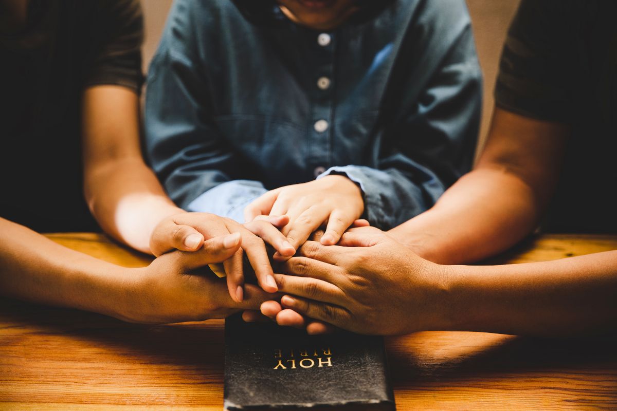 Close-up of family hands joined together in prayer over a Holy Bible, symbolizing love and togetherness in a new year prayer for family.