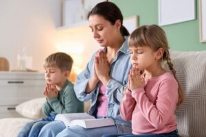 Family sharing peaceful prayers for children together on the couch with an open book.