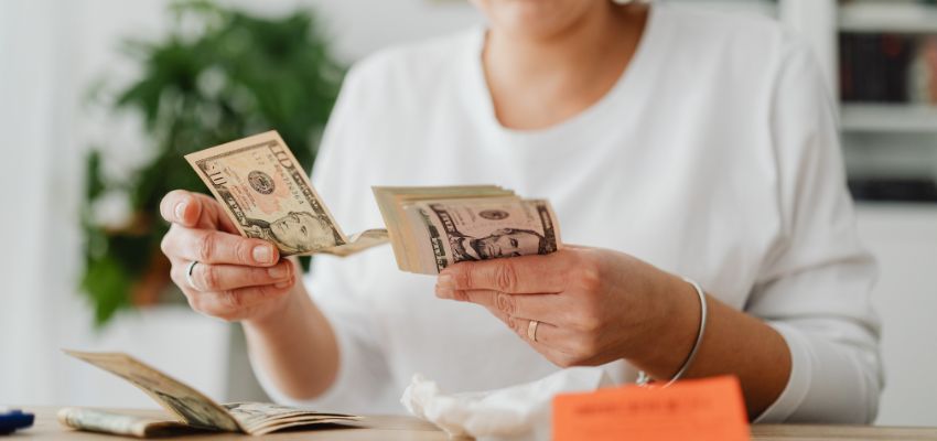 Hands counting US dollar bills, representing what does the bible say about money and financial stewardship.
