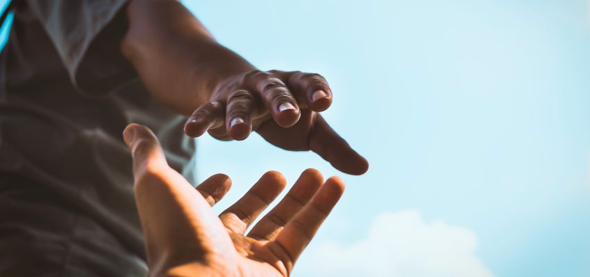 Two hands reaching toward each other against the sky, symbolizing generosity and what does the bible say about money.