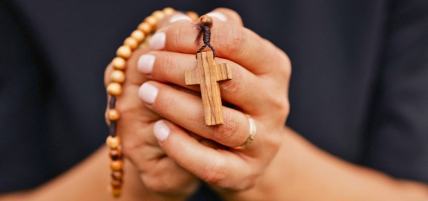 Hands holding a wooden cross and rosary in prayer, turning to bible verses for discouragement for strength and faith