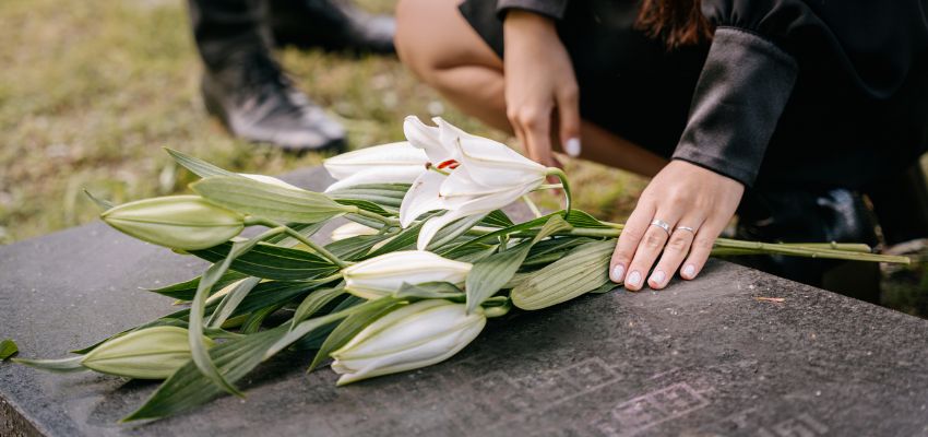 Hand placing white lilies on a gravestone while seeking scripture for loss of loved one.